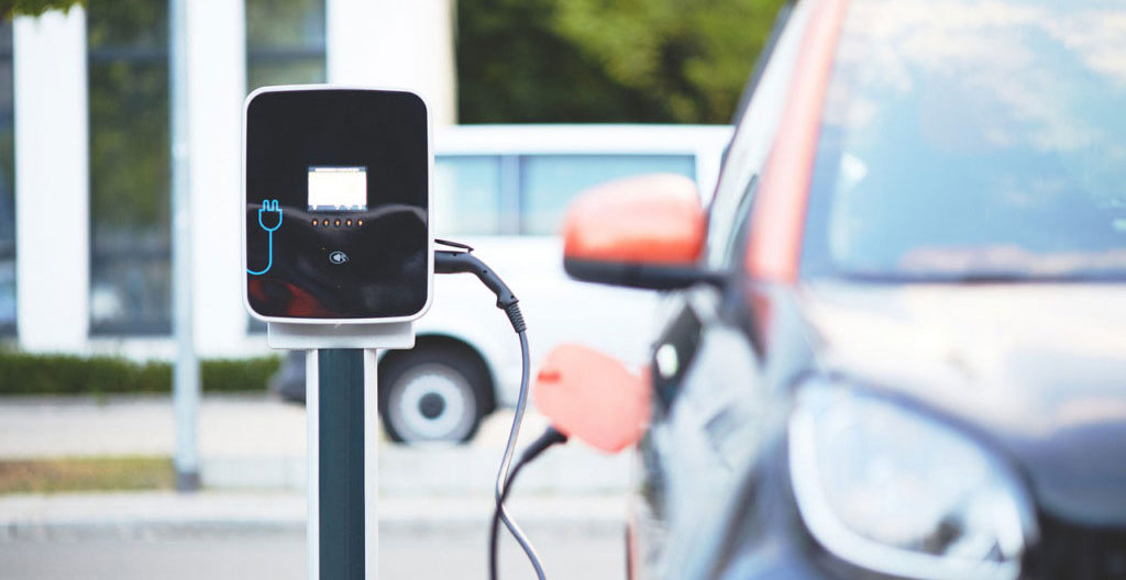 Peugeot e-208 blanche branchée sur borne de recharge publique en contexte urbain français, écran affichant l'état de charge
